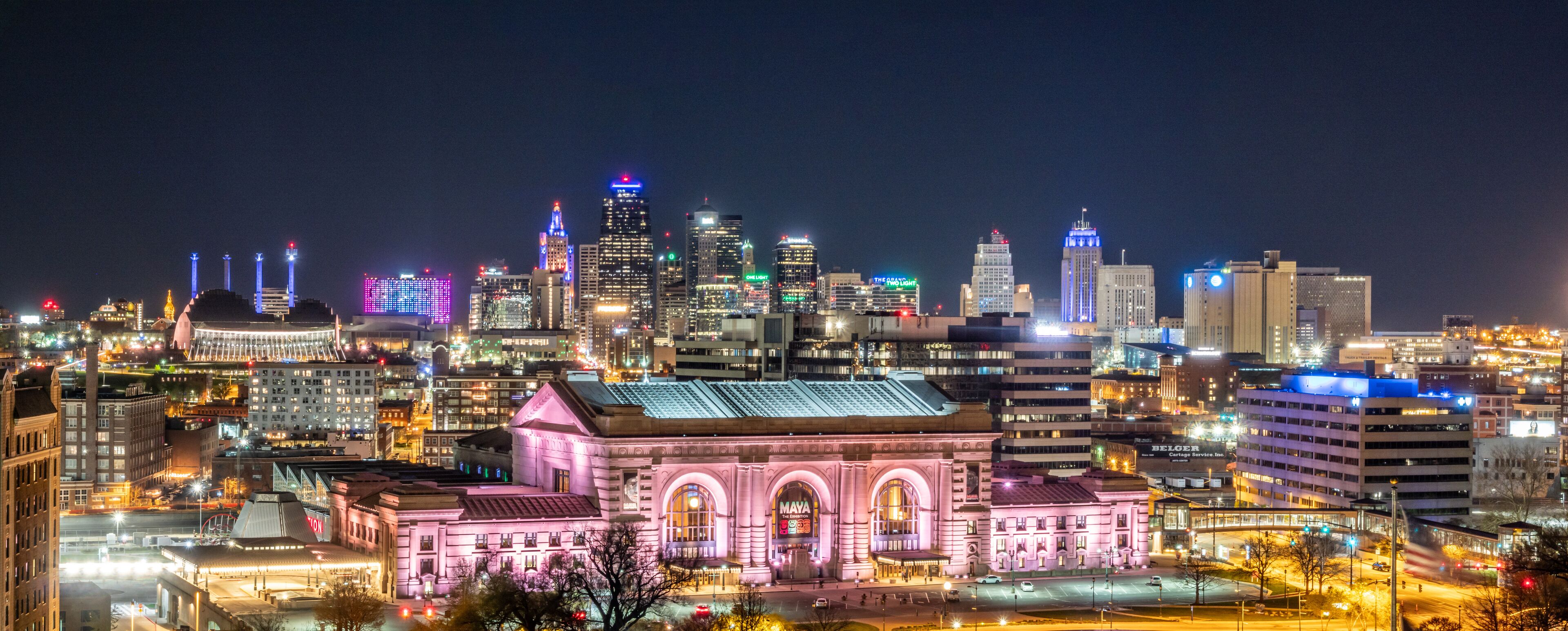 A city skyline at night with illuminated buildings and a prominent pink-lit building in the foreground.