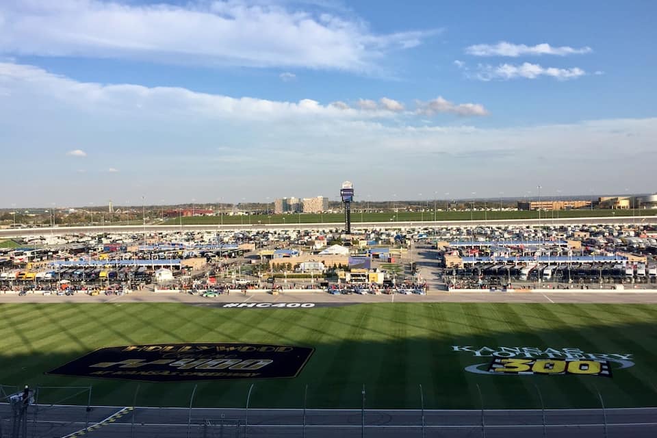 Un grand parking doté d’une piste d’athlétisme, d’un tableau d’affichage et offrant une vue lointaine sur les gratte-ciel d’une ville.