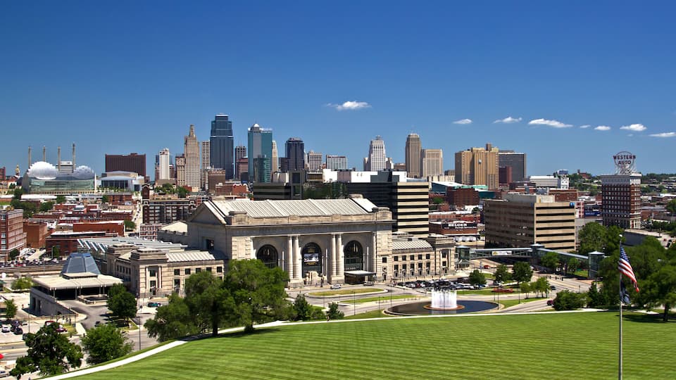 A cityscape with a prominent historic building, modern skyscrapers, and a clear blue sky.