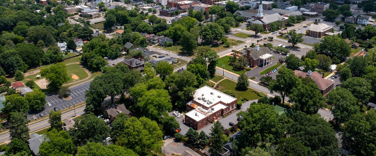An aerial view of a town with a mix of residential and commercial buildings, surrounded by greenery.