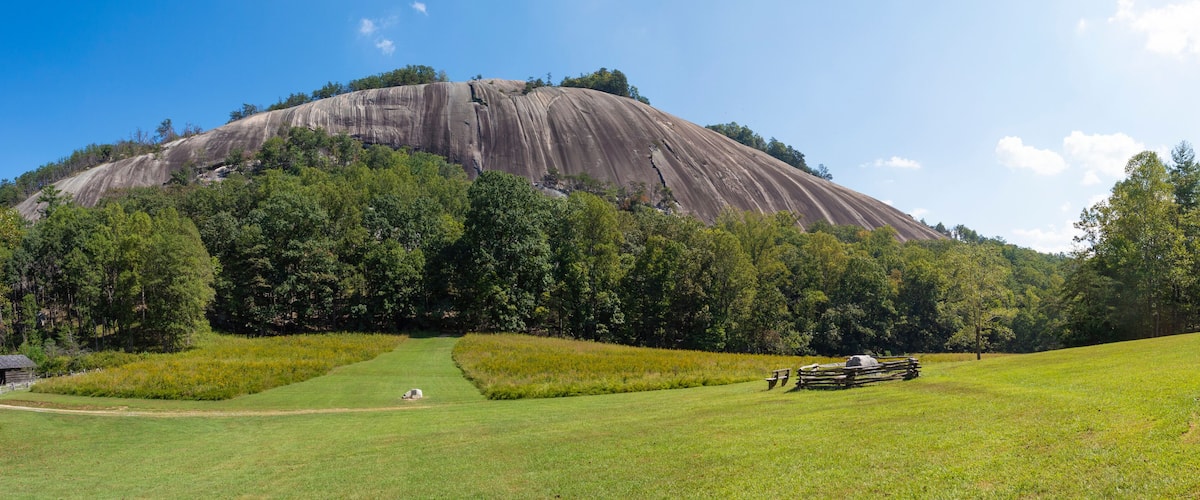 A large rock formation surrounded by lush green trees and a grassy field with a picnic area.