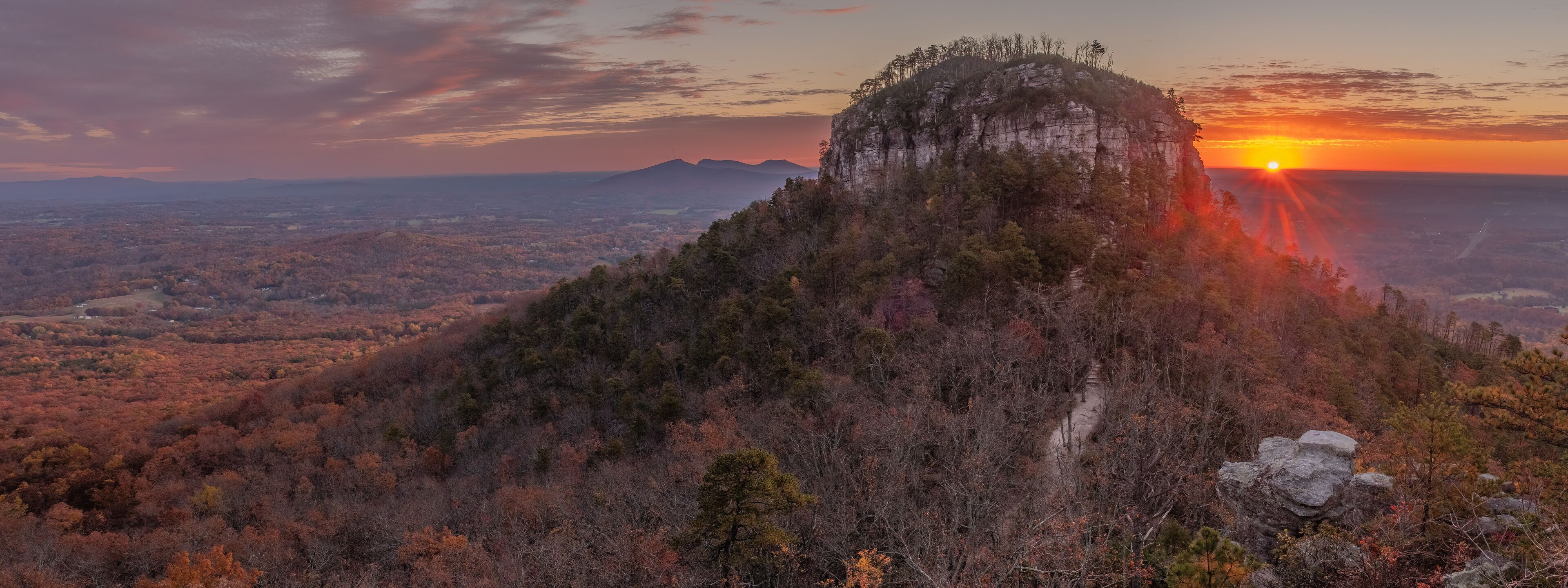 A mountain with a forested peak and a sunset in the background.