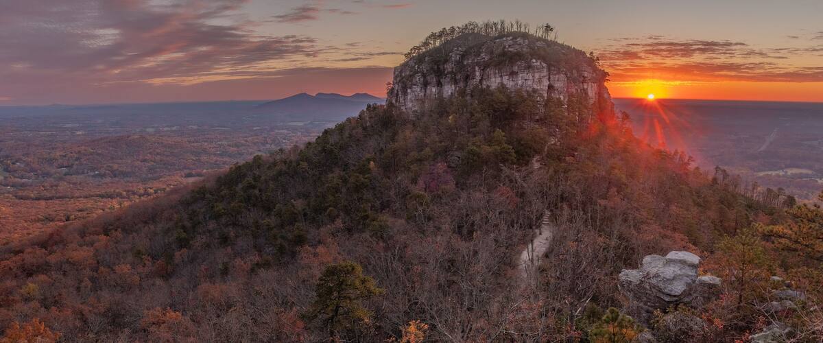 A mountain with a forested peak and a sunset in the background.