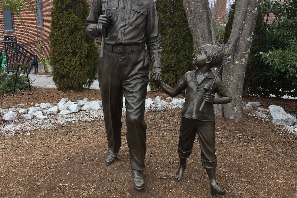 A statue of a man and a child holding hands, with a plaque below.
