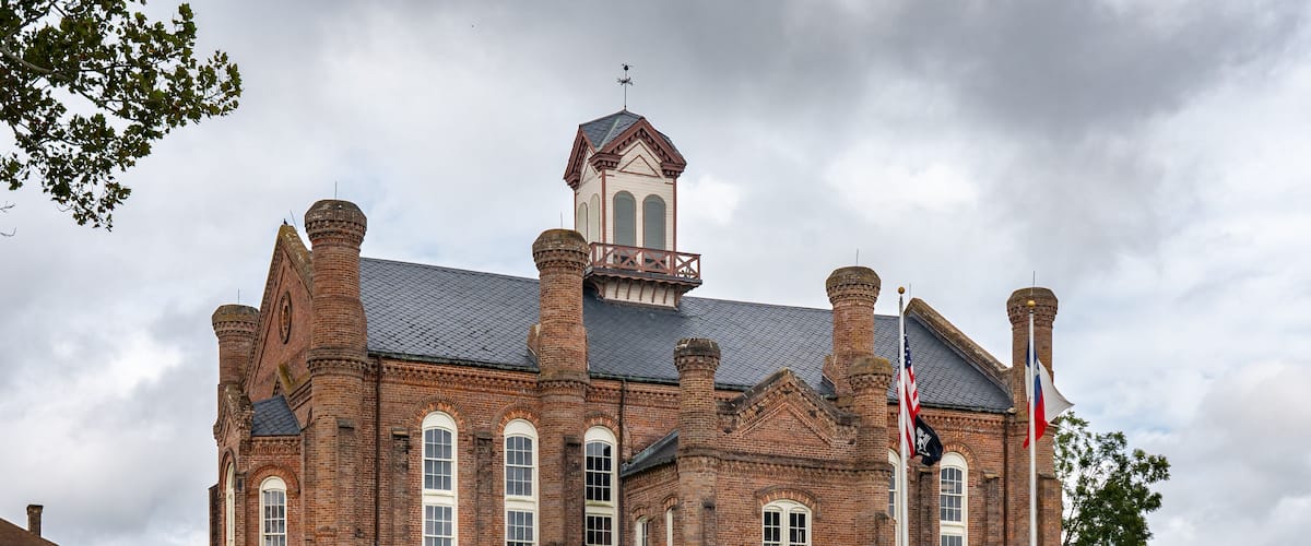 A large brick building with multiple chimneys, a bell tower, and flags.
