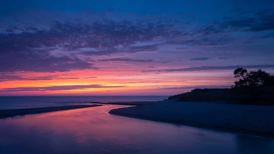 A sunset over a beach with a calm sea reflecting the sky.