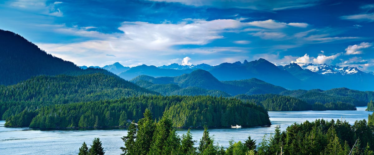 A mountainous landscape with a lake, forested areas, and snow-capped peaks.