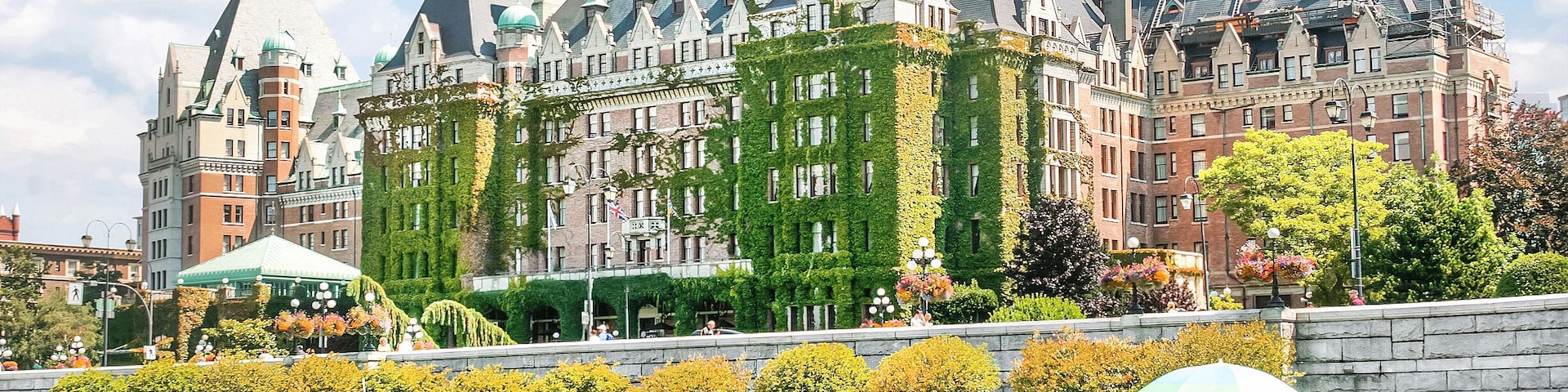 Un edificio histórico con hiedra verde, una embarcación en el agua y personas caminando por la orilla.