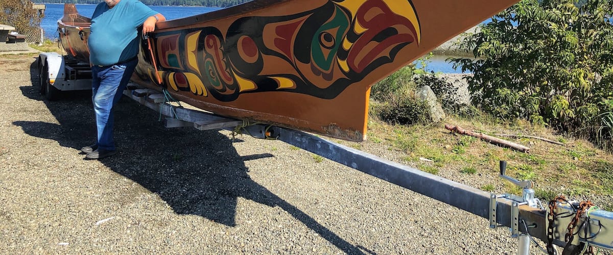 A man holding a canoe with a painted design.