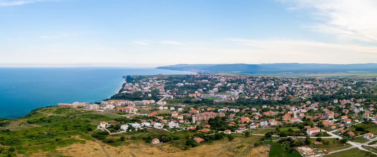 A coastal town with a mix of residential buildings and open green spaces, overlooking the sea.