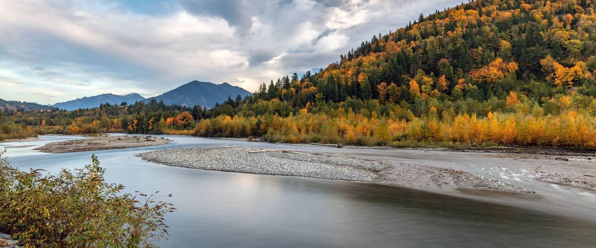 A river winding through a forested valley with autumn foliage and distant mountains.