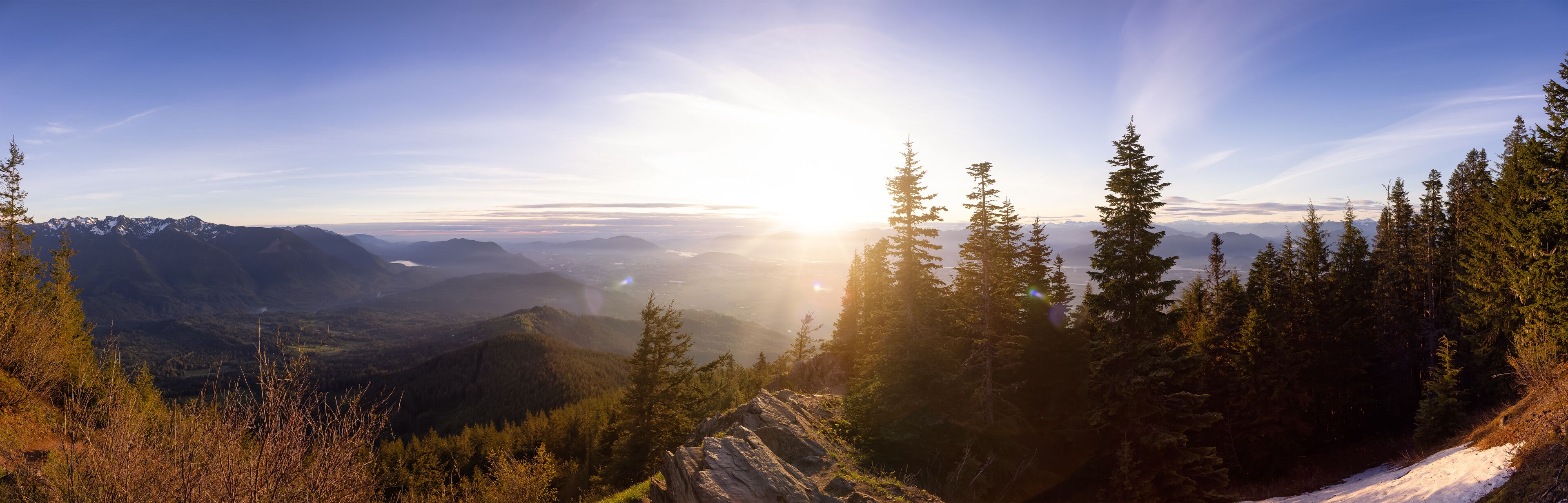 A mountainous landscape with a clear sky and sunlight filtering through trees.