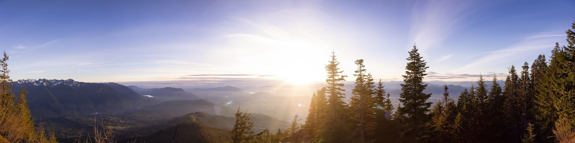 A mountainous landscape with a clear sky and sunlight filtering through trees.