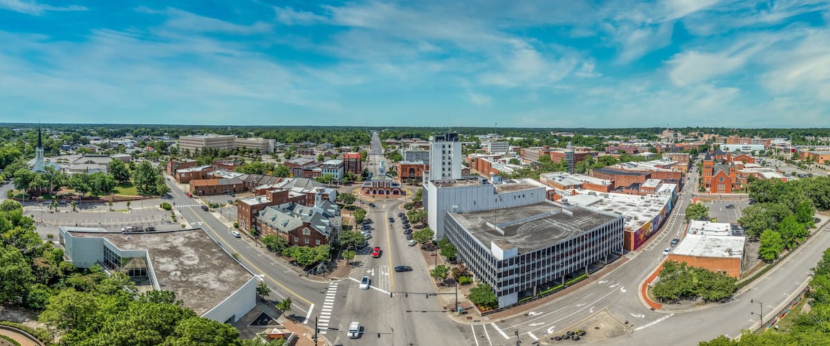 A cityscape with a mix of historic and modern buildings, a prominent church steeple, and a large parking lot.