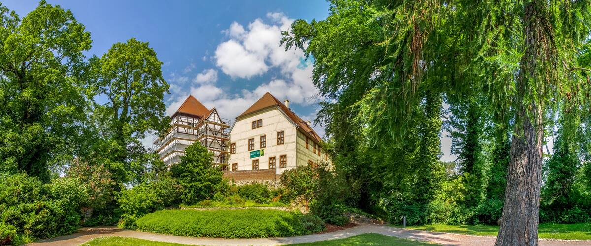 A historic building with a traditional European architectural style, surrounded by lush greenery and trees.