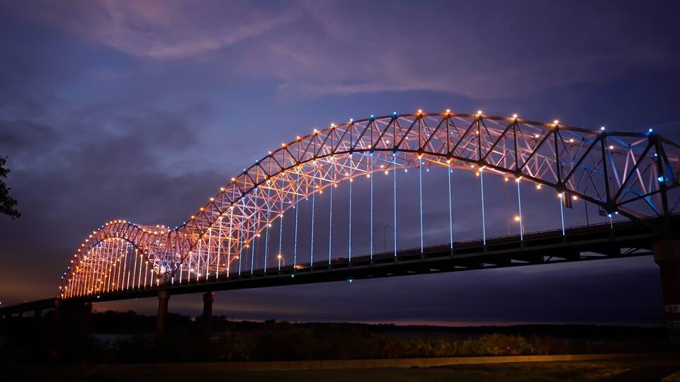 A brightly lit bridge with a distinctive arch design, featuring numerous lights along its structure.