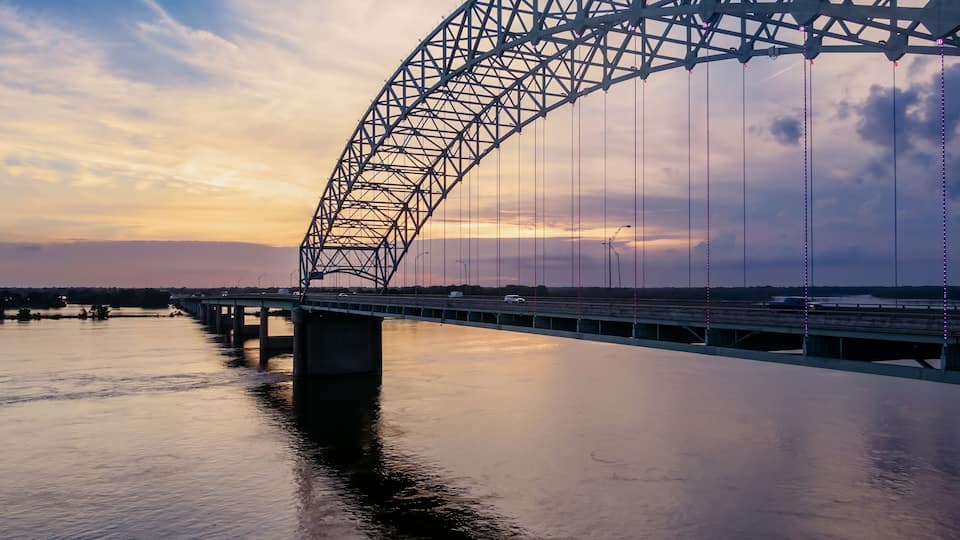 A large steel bridge spanning a river at sunset.