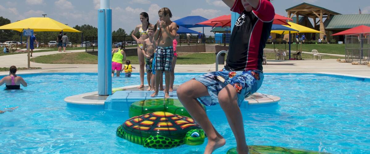 A swimming pool with people, a turtle float, and a rope climbing structure.