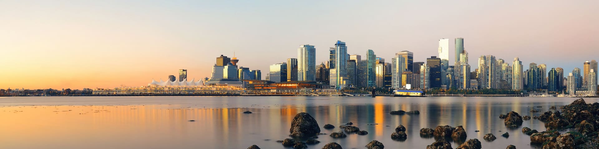 A city skyline at sunset with a calm river in the foreground.
