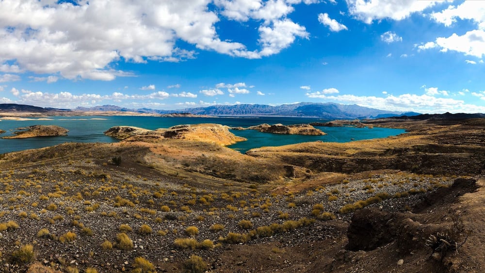 A rugged landscape with a large body of water, rocky terrain, and distant mountains under a partly cloudy sky.