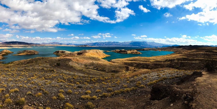 A rugged landscape with a large body of water, rocky terrain, and distant mountains under a partly cloudy sky.