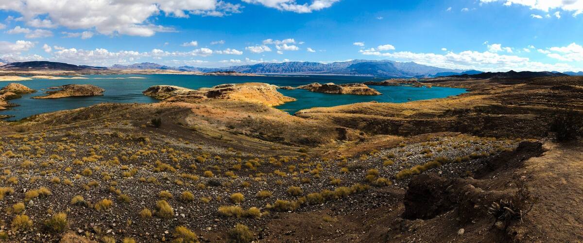 A rugged landscape with a large body of water, rocky terrain, and distant mountains under a partly cloudy sky.