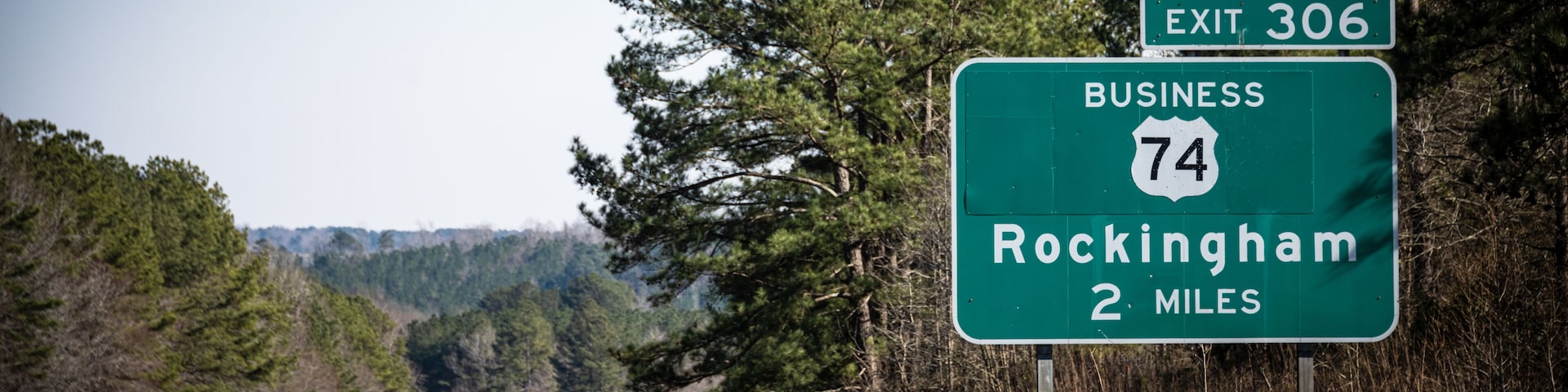 Placa de saída rodoviária para a Saída 306, Rodovia Comercial 74, indicando que Rockingham está a 3 quilômetros à frente.