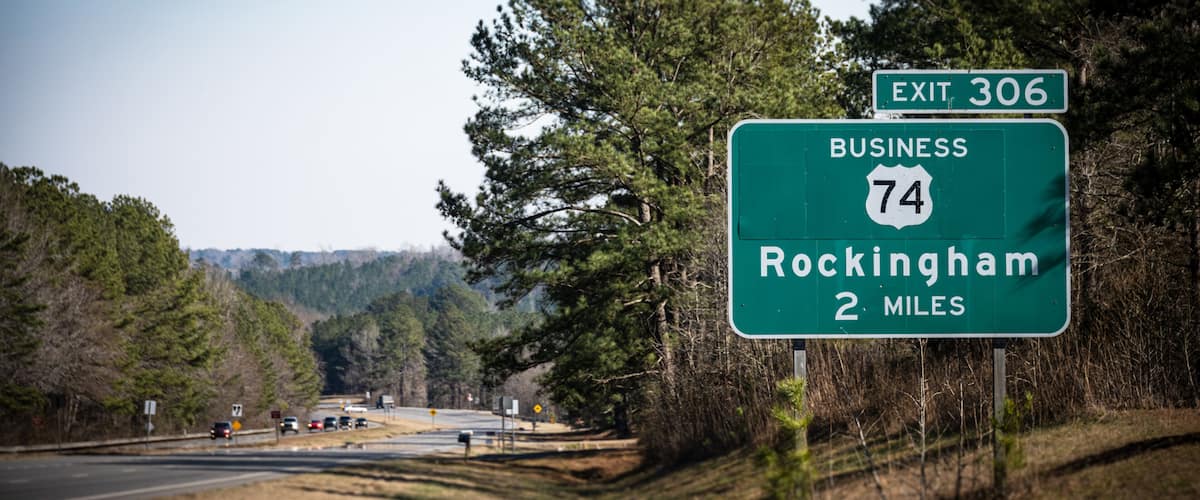 A highway exit sign for Exit 306, Business 74, indicating Rockingham is 2 miles ahead.