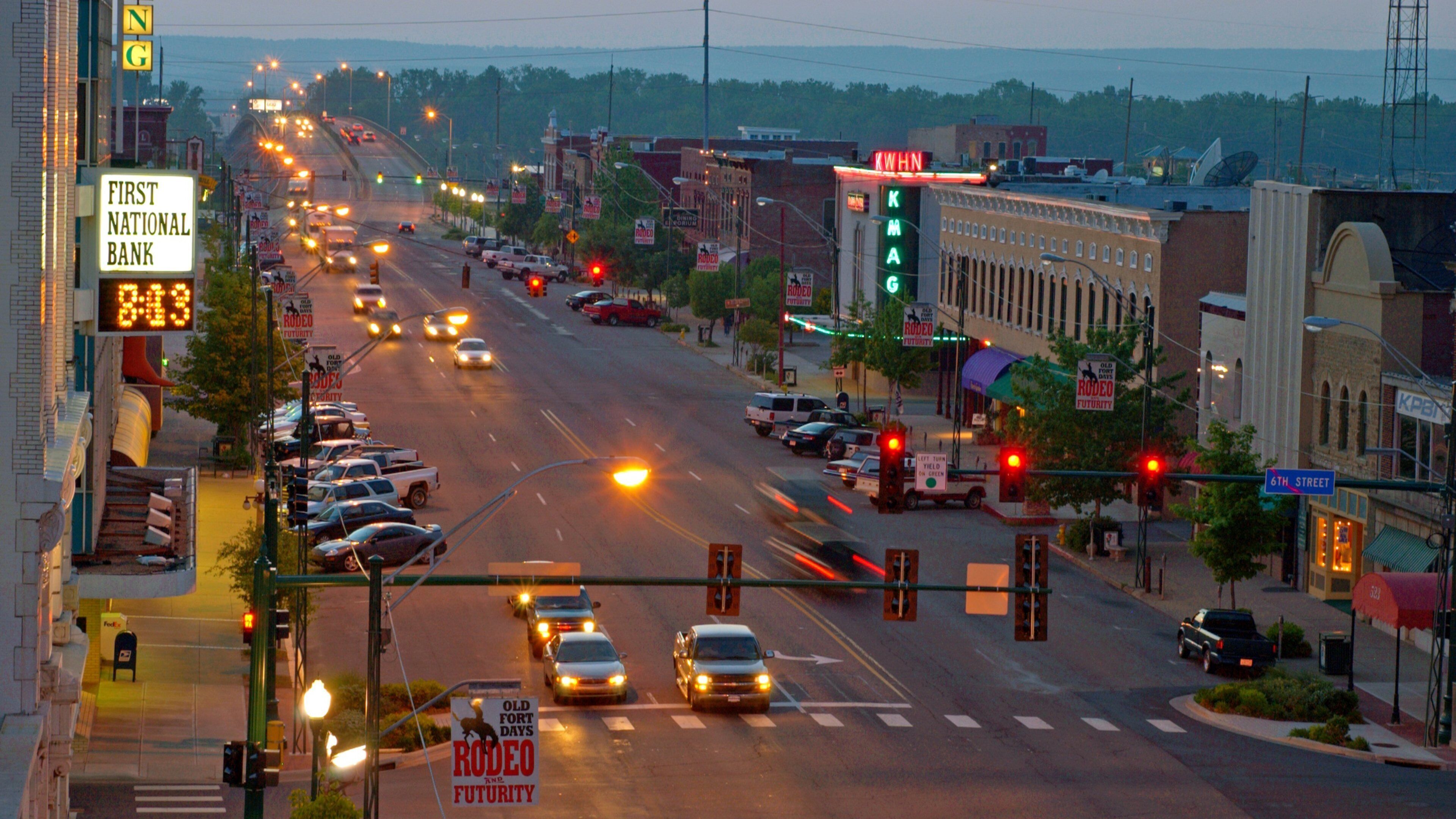 A busy street with cars, traffic lights, and various signs including 'First National Bank' and 'Rodeo Futurity'.