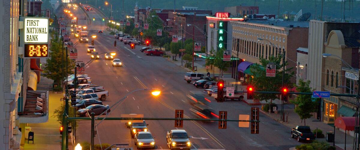 A busy street with cars, traffic lights, and various signs including 'First National Bank' and 'Rodeo Futurity'.