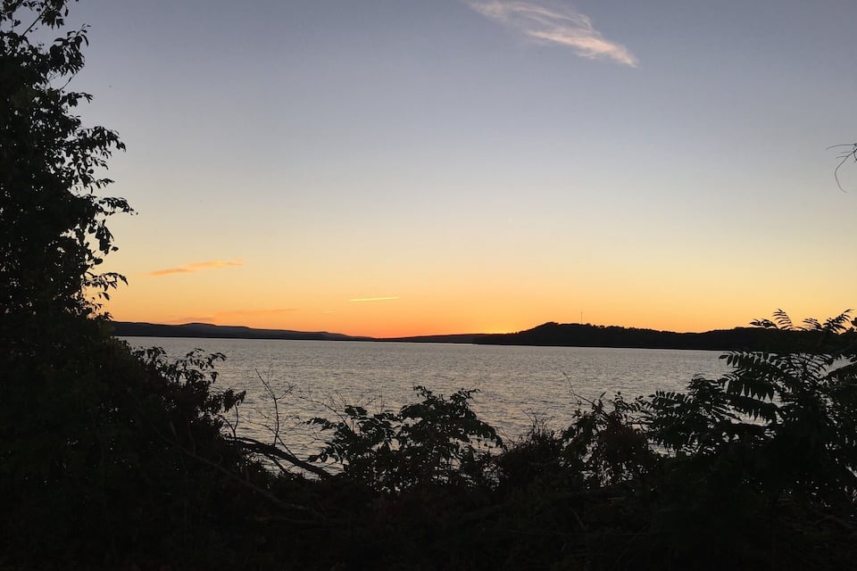 A sunset over a calm lake with silhouettes of trees and distant hills.