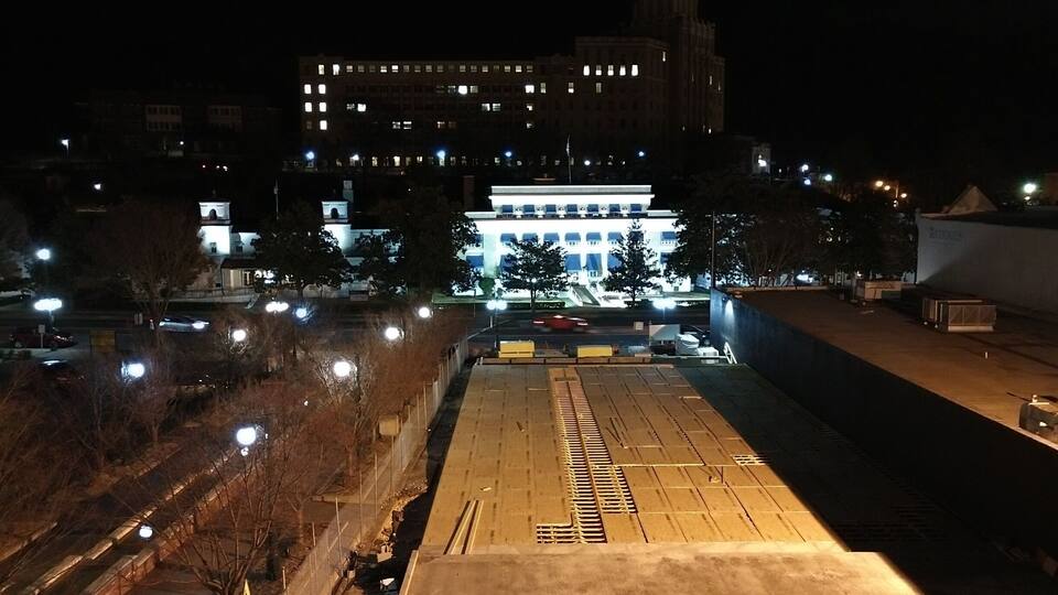 A nighttime view of a cityscape with illuminated buildings and a parking lot.