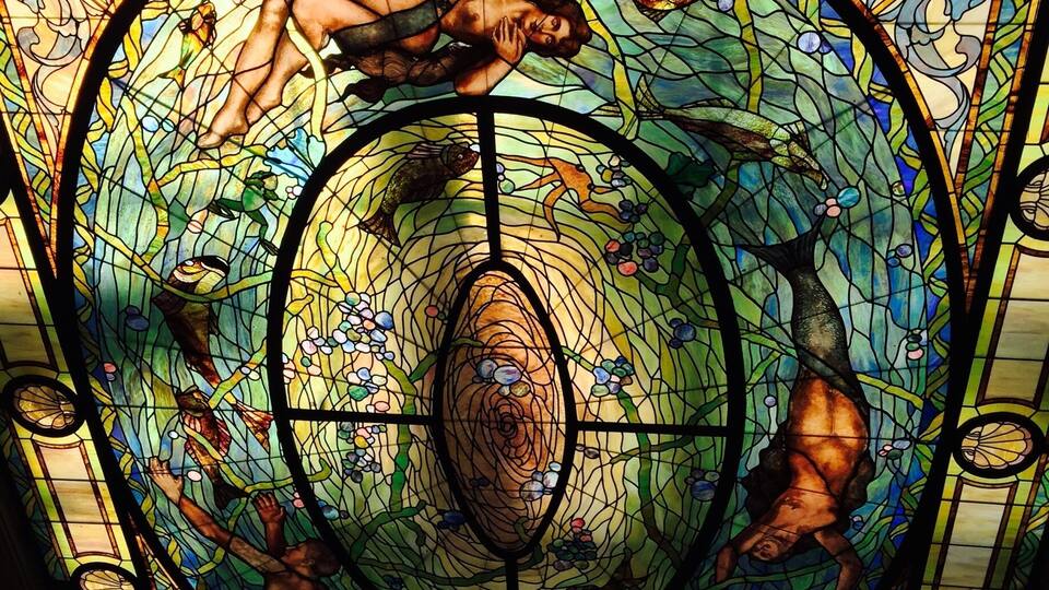 A stained glass window with a central circular design, surrounded by various figures and patterns.