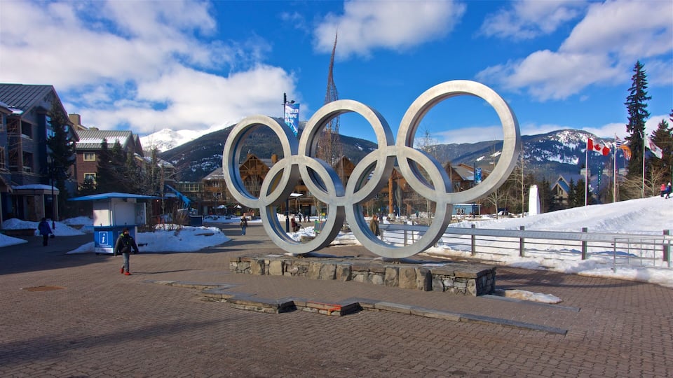 En stor skulptur af de olympiske ringe i en snedækket by med bjerge i baggrunden.