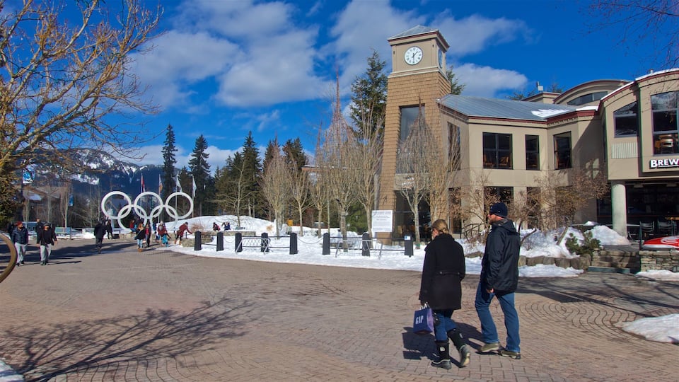 A snowy plaza with the Olympic rings sculpture, a clock tower, and a building with a 'Brewery' sign.