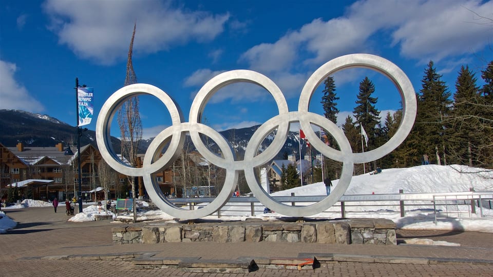 A large Olympic rings sculpture in a snowy setting with mountains in the background.