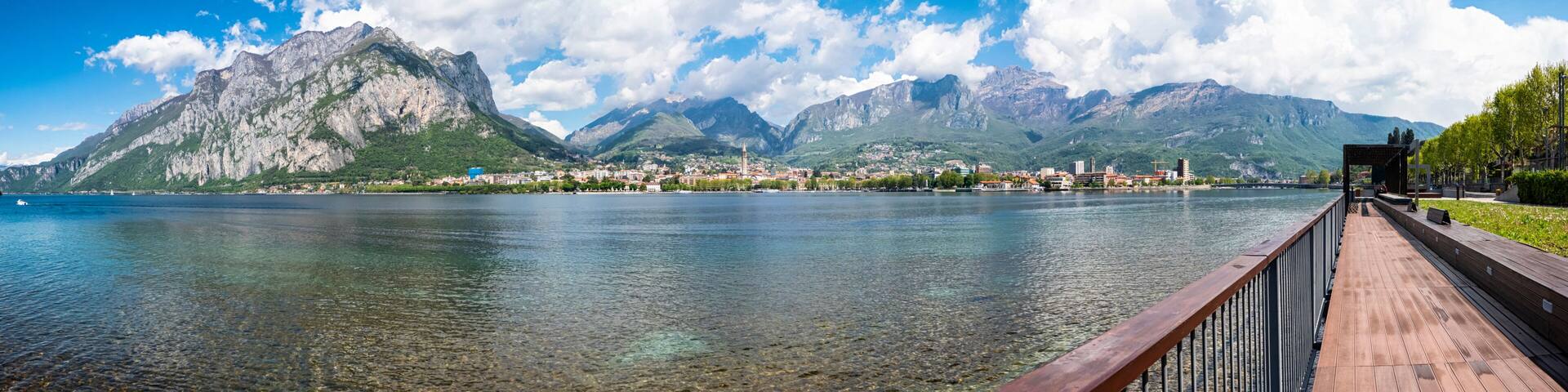 A lake with a wooden walkway, mountains in the background, and a town across the water.