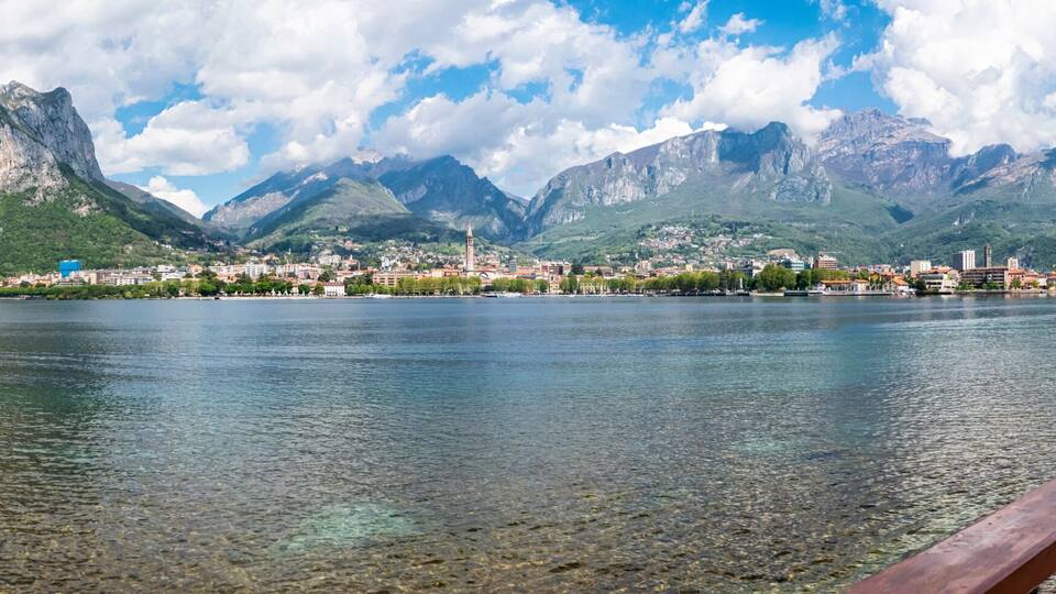 A lake with a wooden walkway, mountains in the background, and a town across the water.