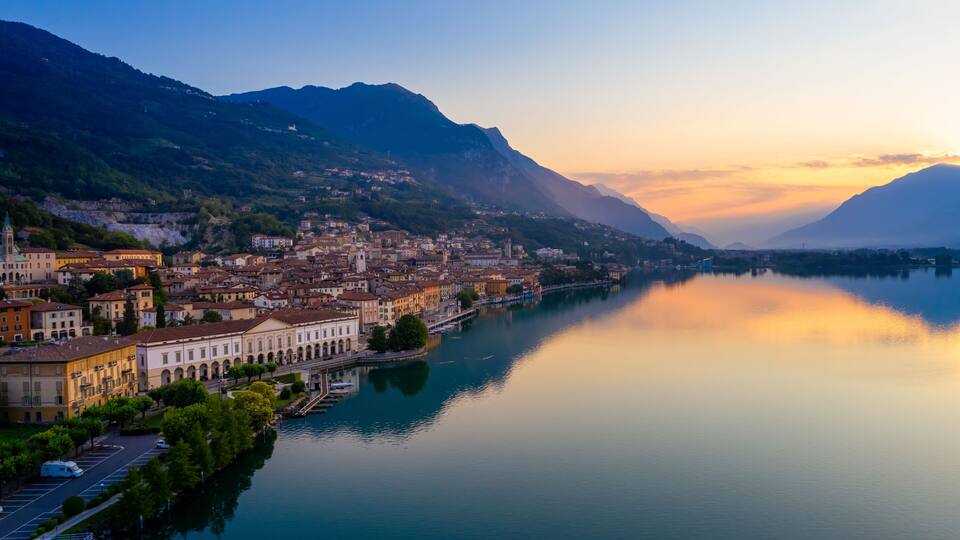 A lakeside town with historic buildings, a church, and mountains in the background.