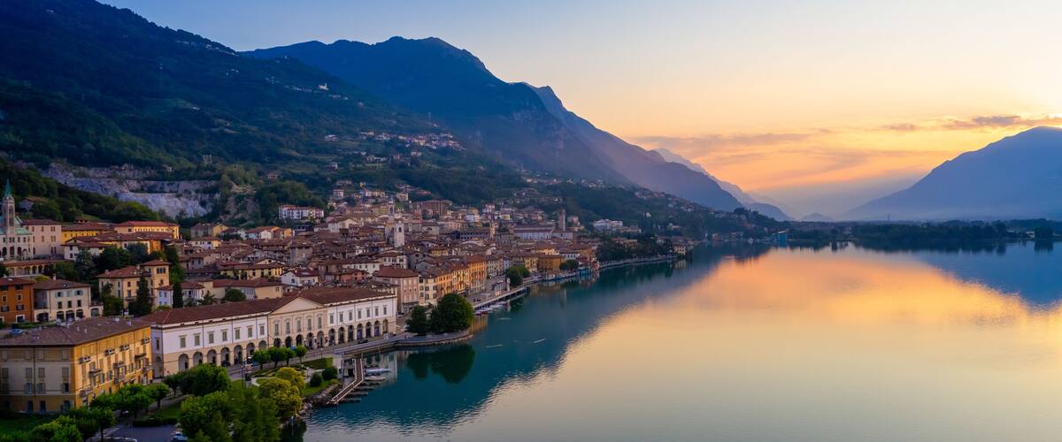 A lakeside town with historic buildings, a church, and mountains in the background.
