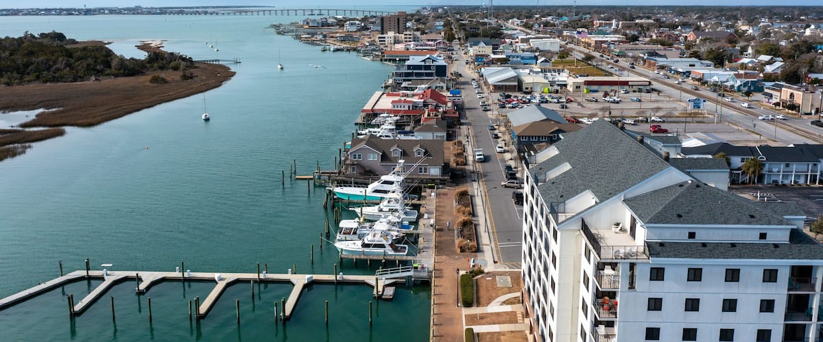 A marina with boats docked, a bridge in the distance, and a town with buildings and roads.