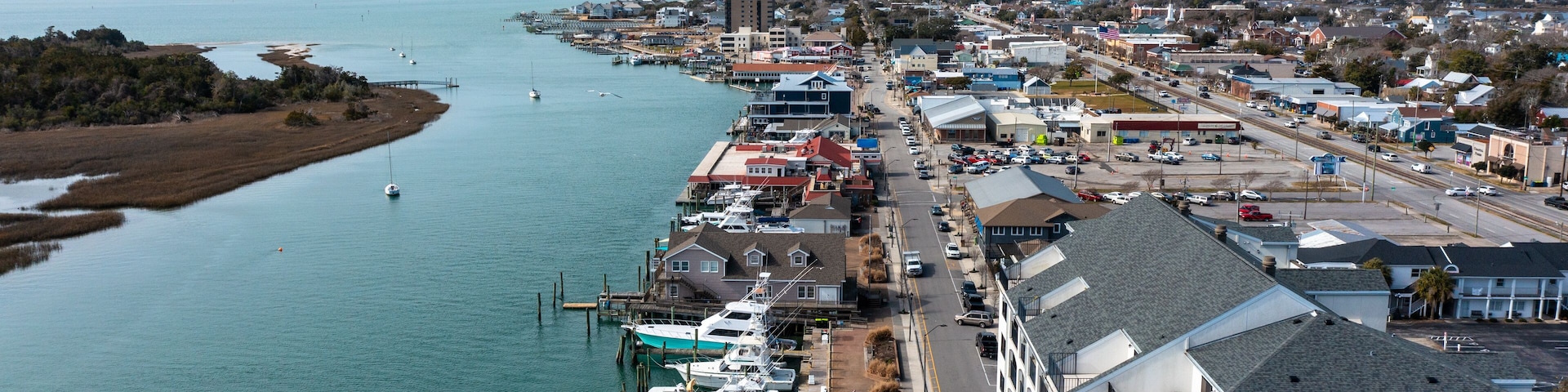 A marina with boats docked, a bridge in the distance, and a town with buildings and roads.