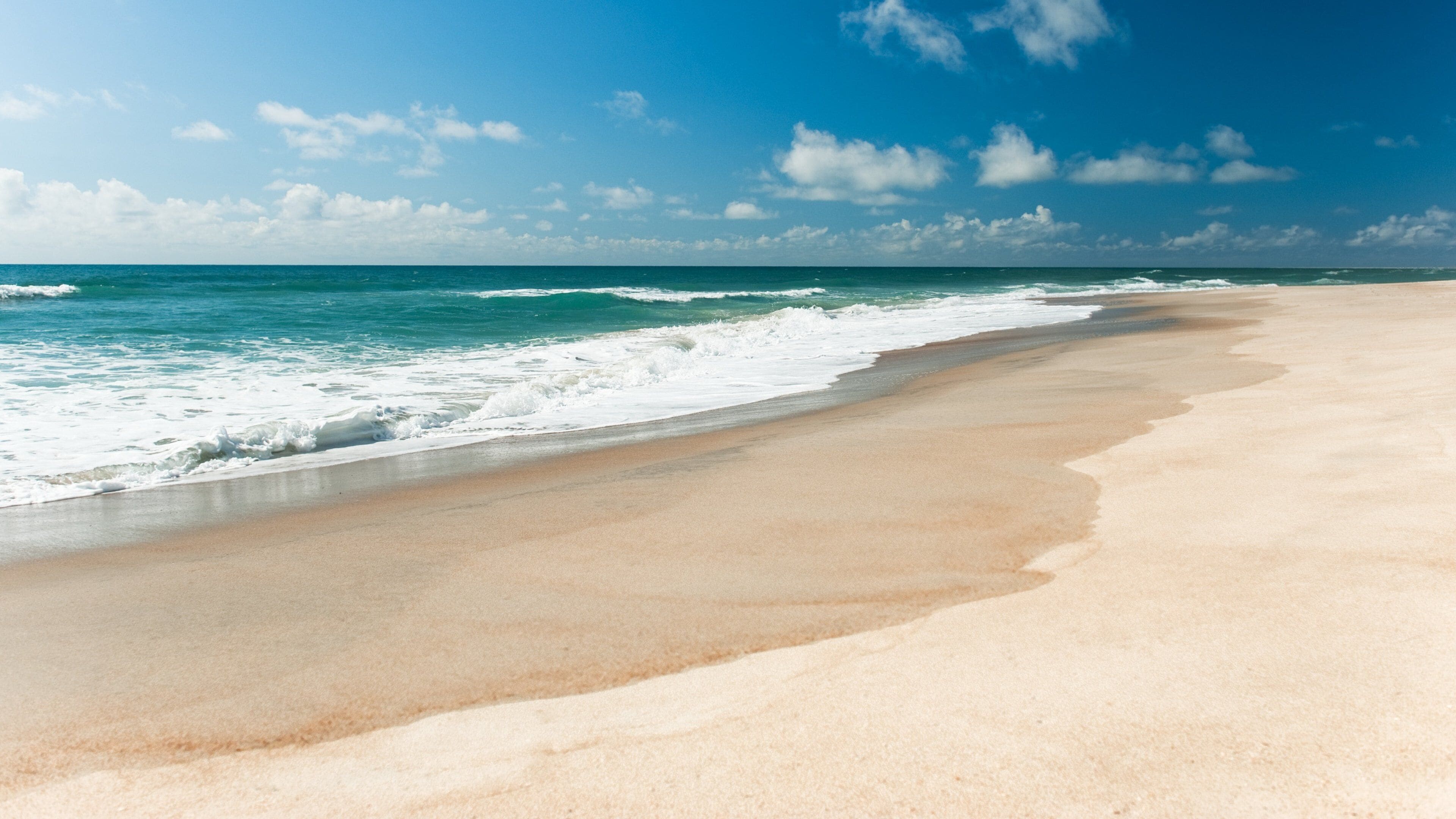 A sandy beach with waves crashing onto the shore under a clear blue sky.