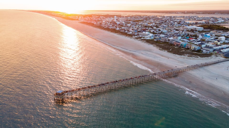 A coastal town with a pier extending into the sea, surrounded by sandy beaches and residential buildings.