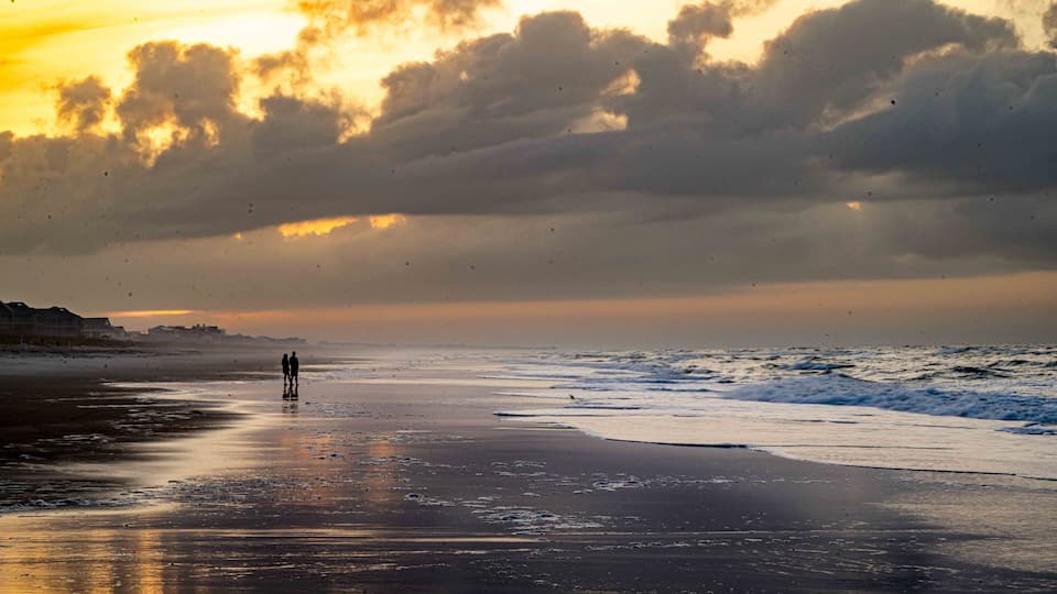 A beach with a sunset, waves, and a distant shoreline.
