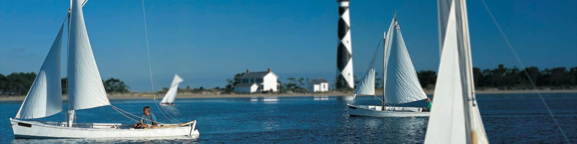 Sailboats on calm water with a lighthouse in the background.