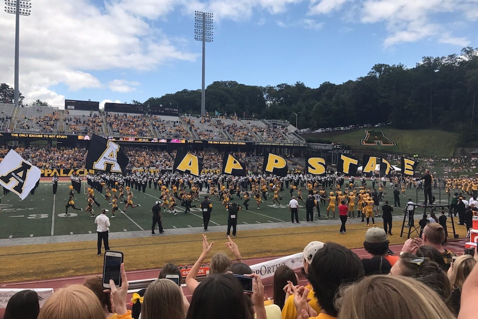 A football field with a marching band and cheerleaders performing.