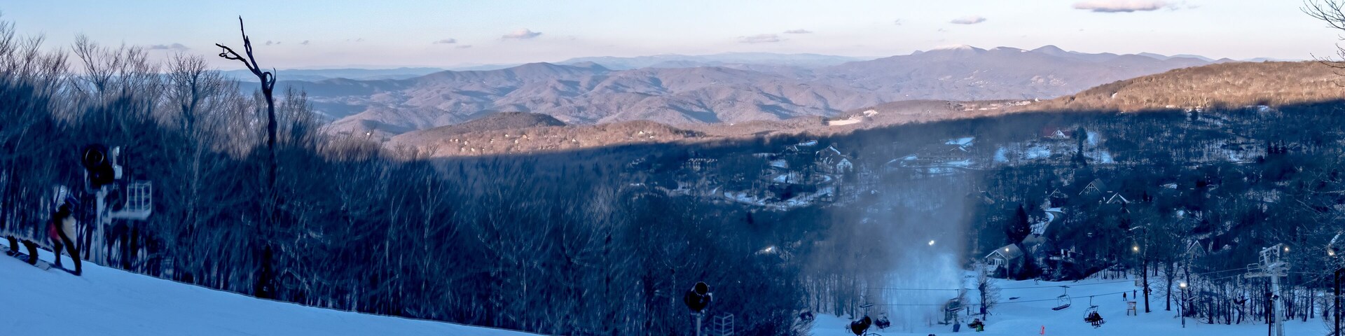 Pista de esquí cubierta de nieve con esquiadores, un telesilla y un paisaje montañoso al fondo.