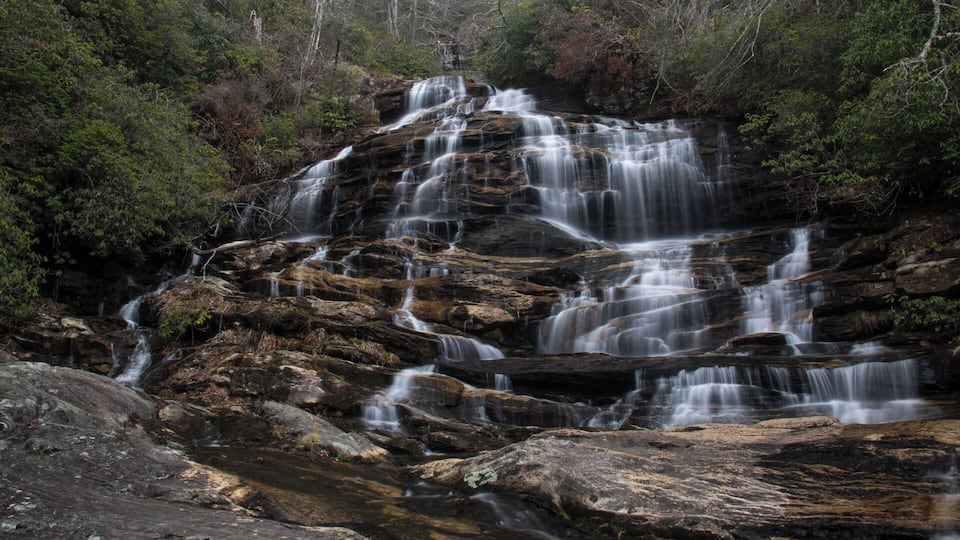 A multi-tiered waterfall surrounded by dense forest.