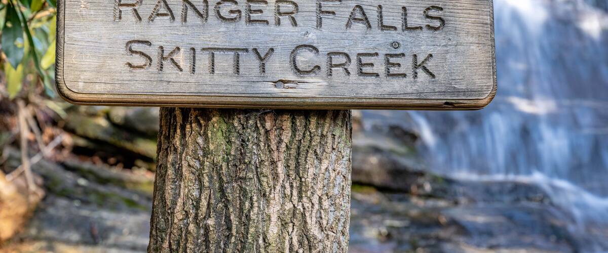 A wooden sign with 'RANGER FALLS SKITTY CREEK' engraved on it, mounted on a tree.